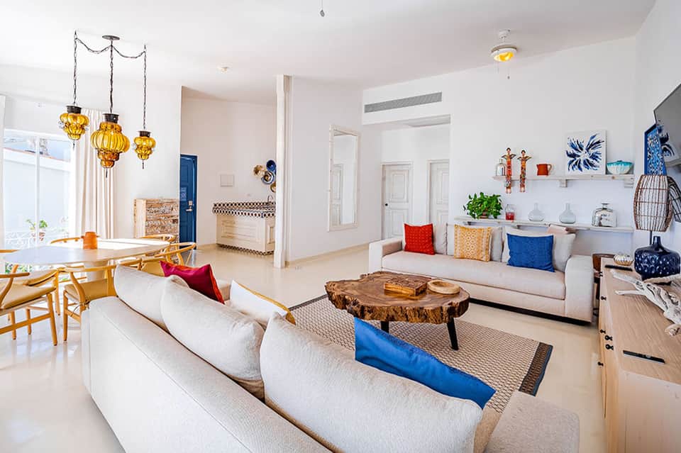 Bright modern living room with cream sofas, wooden furniture, blue accents, and golden hanging light fixtures