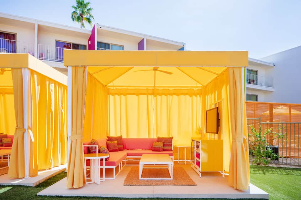 Bright yellow cabana with coral cushions, white tables, and flowing curtains in resort courtyard