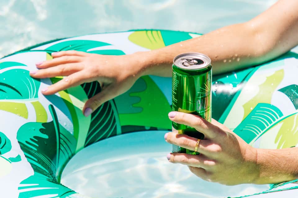 Person holding beverage float in swimming pool with tropical leaf pattern