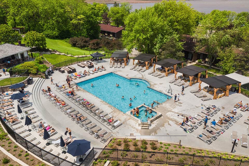 Aerial view of resort pool complex surrounded by lounge chairs, umbrellas, and forested grounds