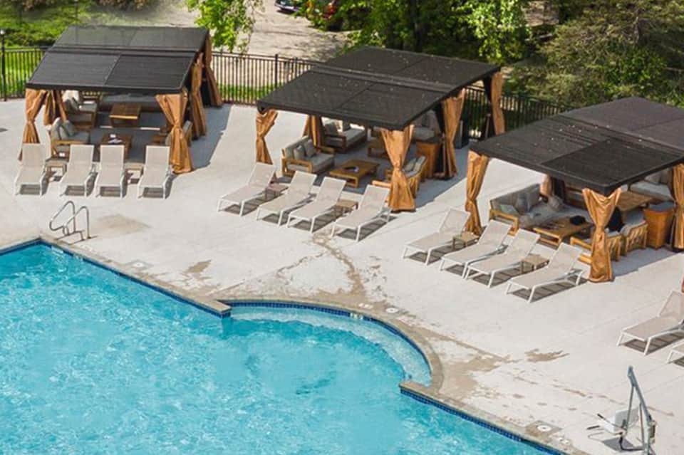 Resort pool with wooden cabanas, white lounge chairs, and lush green landscape surroundings