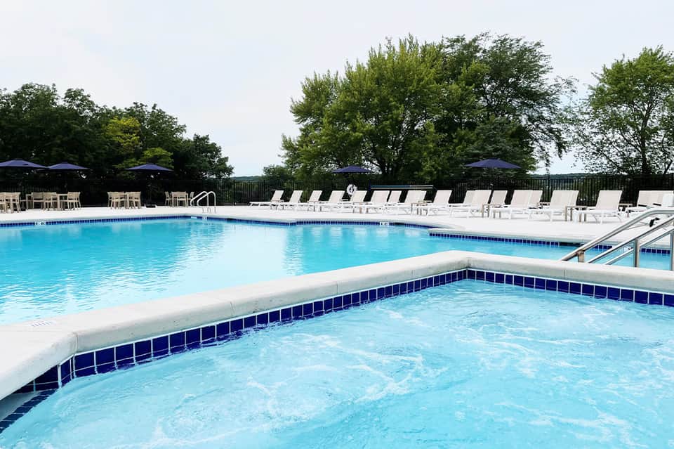 Outdoor pool with spa feature, loungers with umbrellas, and tree-lined landscape