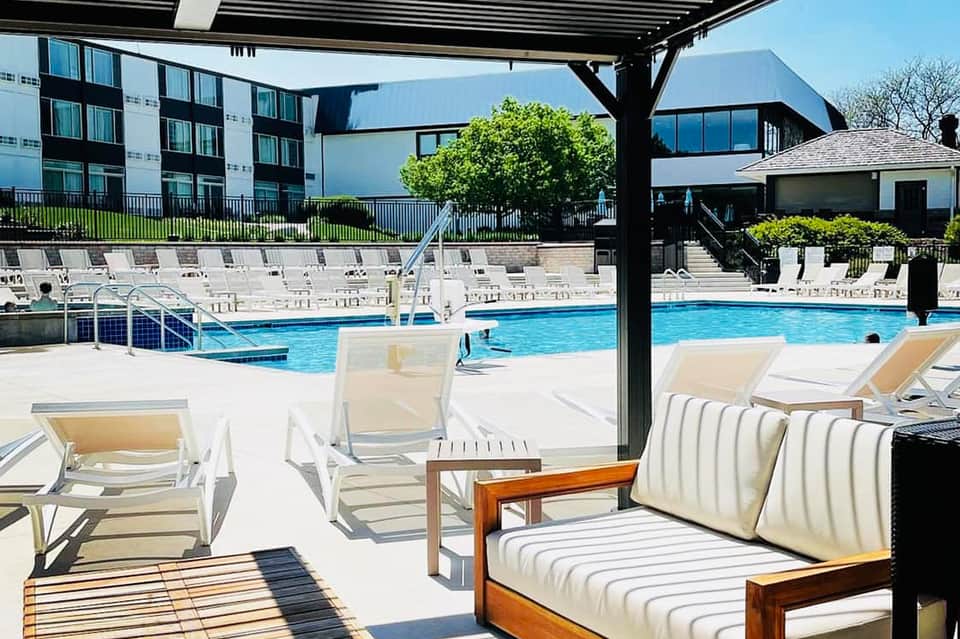 Resort pool area with white lounge chairs, pergola shade structure, and modern building backdrop