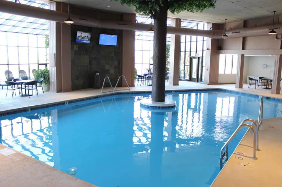 Indoor heated swimming pool with columns, lounge seating, and large windows