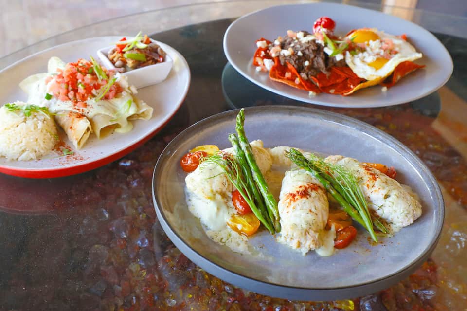 Three plates of gourmet seafood dishes with garnishes and sides on dark table