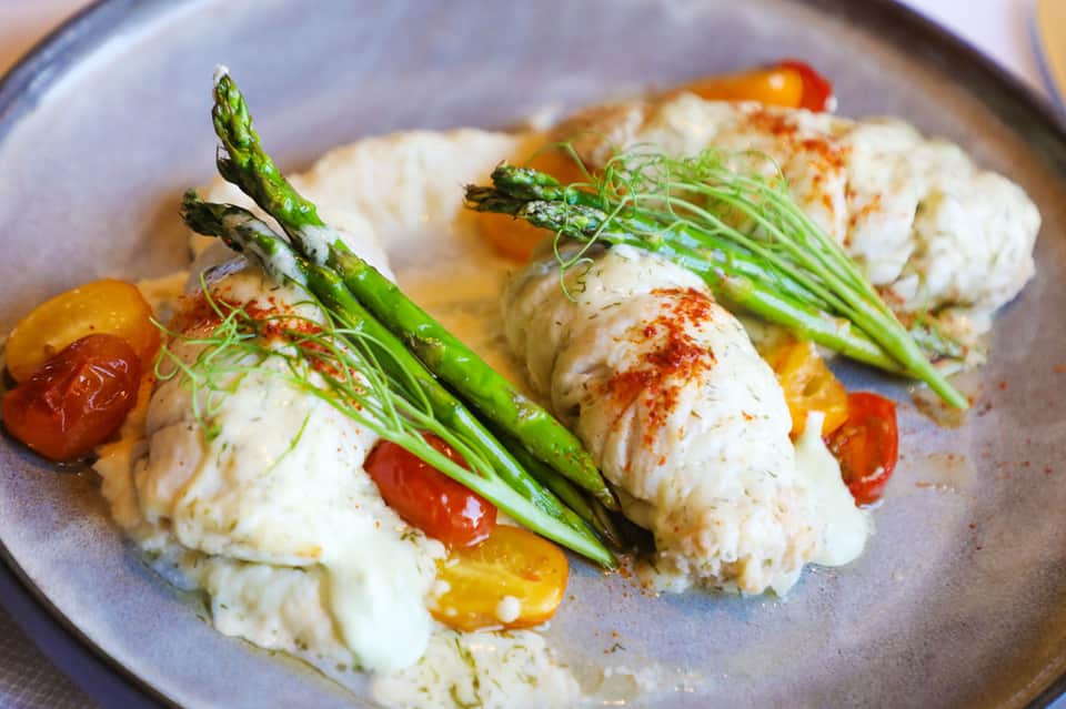 Plated fine dining dish with white protein, green asparagus, and red pepper garnish