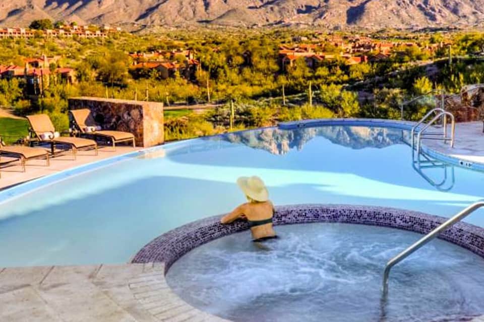 Resort pool with hot tub in foreground, mountain views, desert landscape, and lounge chairs