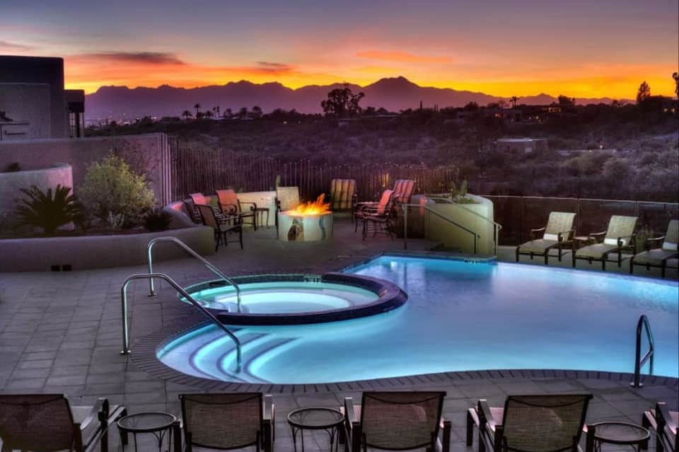 Illuminated resort pool and spa at dusk with firepit, mountain sunset views