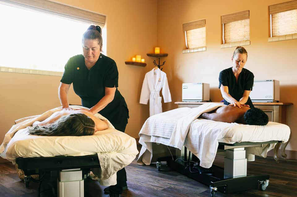 Spa treatment room with two therapists performing massages on clients