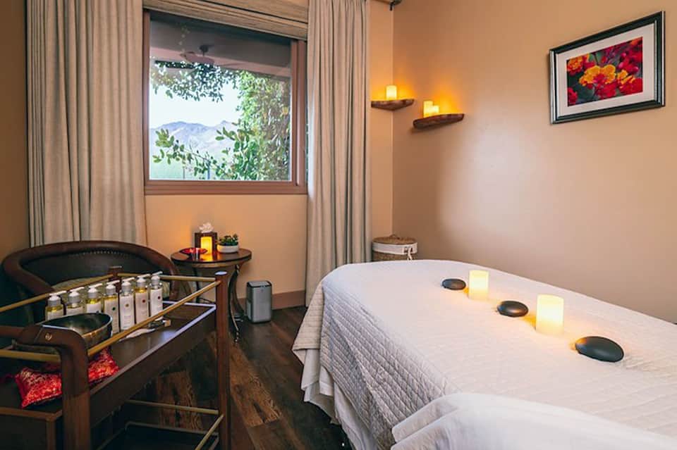 Spa treatment room with massage table, heated stones, candles, window overlooking water