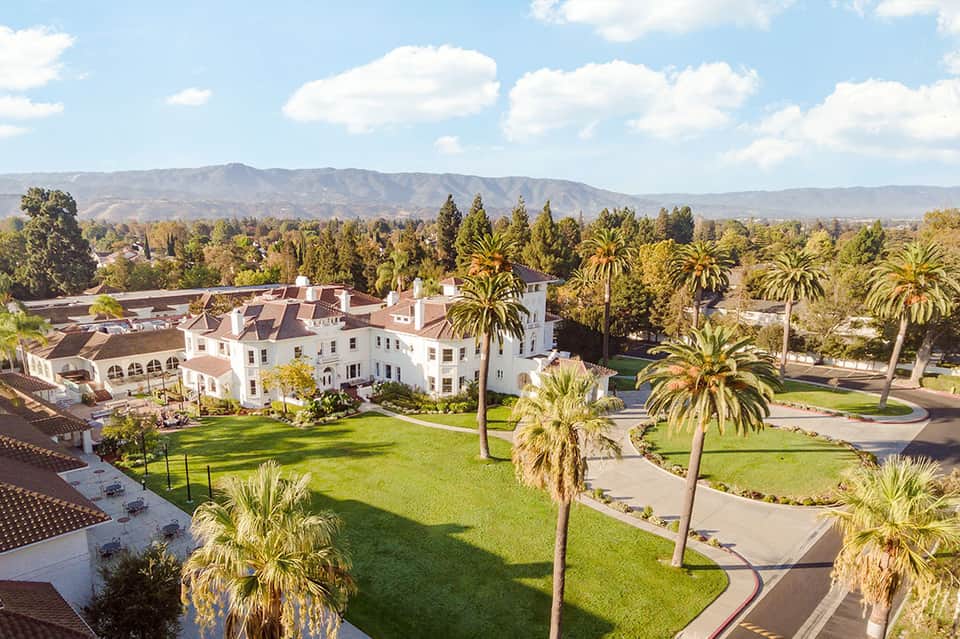 Aerial view of Mediterranean-style white mansion with palm trees and manicured grounds