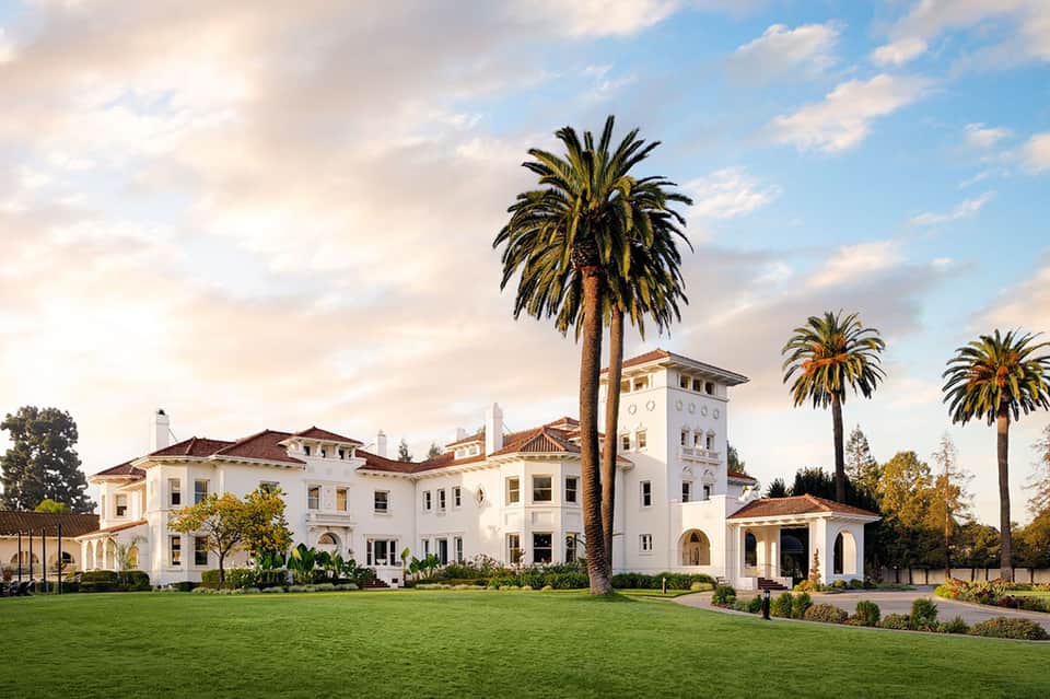 Spanish colonial-style white mansion with tower, palm trees, and manicured green lawn