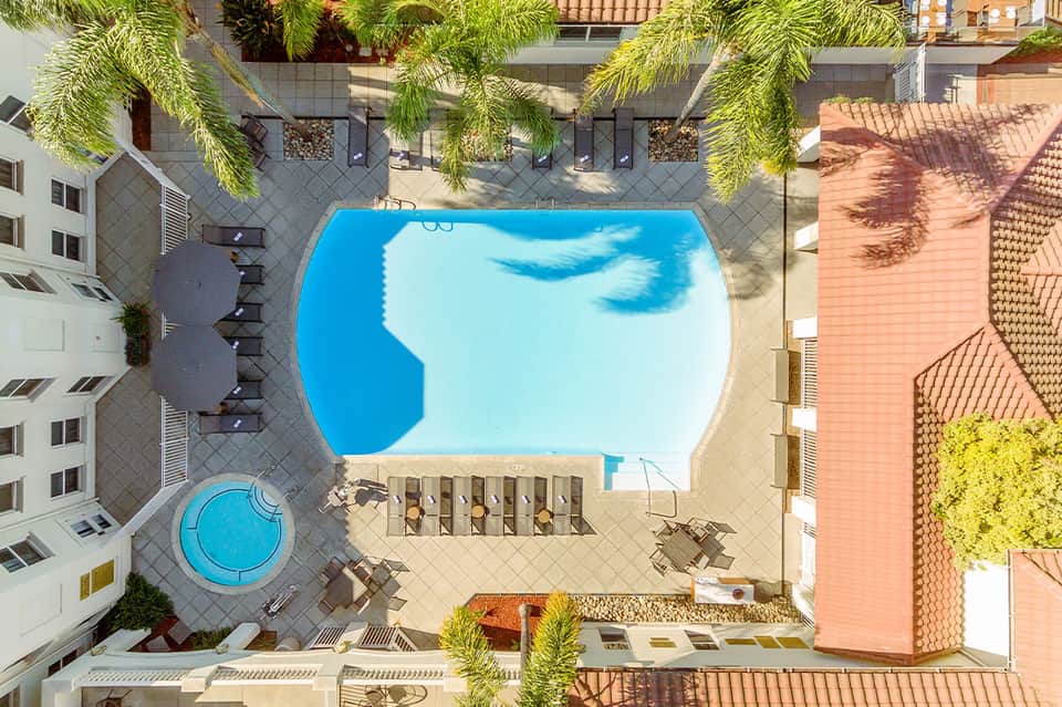 Aerial view of resort pool surrounded by palm trees and residential buildings with blue sky reflection