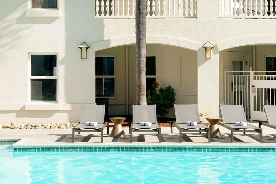 Poolside loungers against white building with arches and palm tree at upscale resort