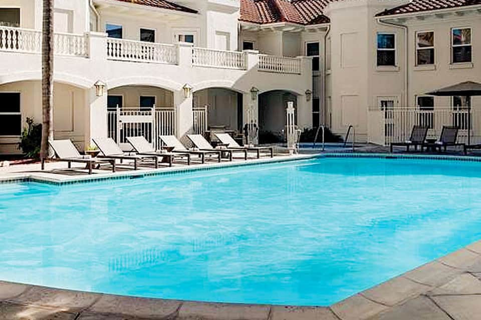 Resort swimming pool with white building colonnade, arches, lounge chairs, and palm tree