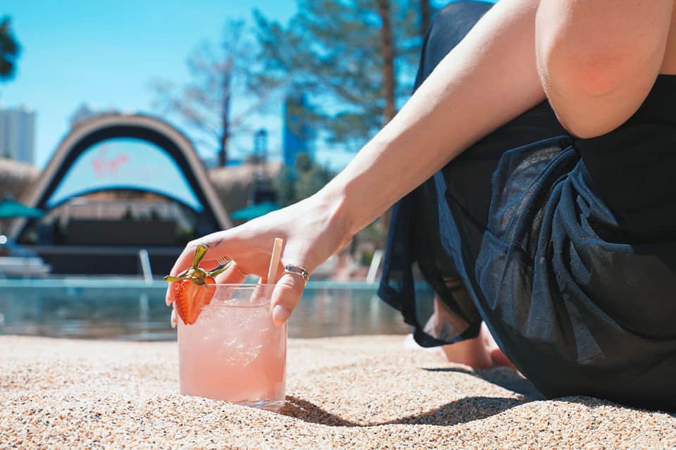 Woman holding pink cocktail by resort pool with city skyline and architectural structures in background