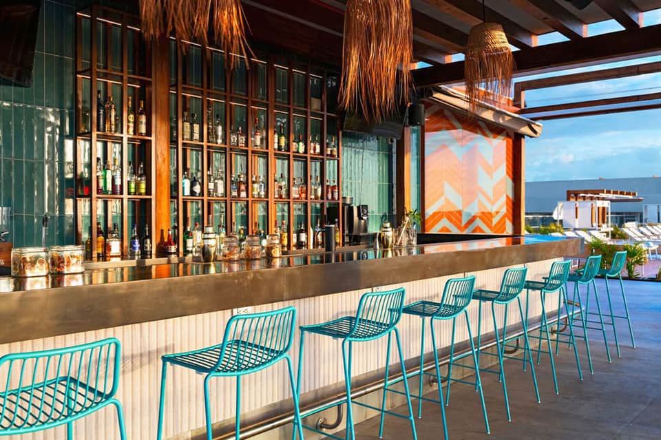Upscale bar with turquoise seating, green-framed liquor cabinets, and ocean views through windows
