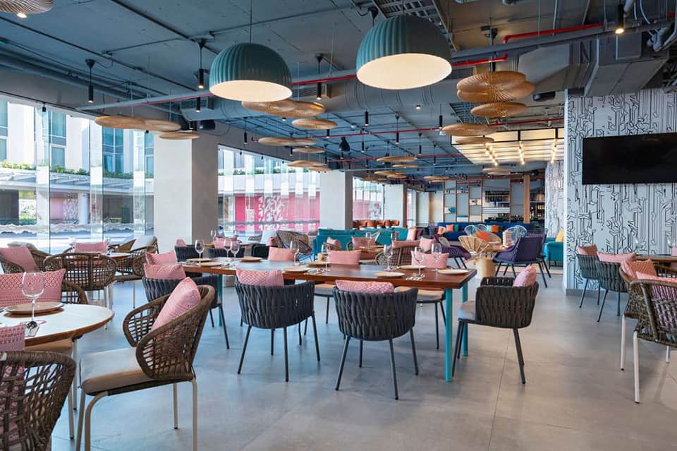 Contemporary restaurant dining area with pink chairs, wood tables, and pendant lighting