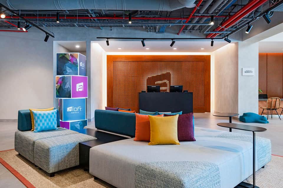Contemporary hotel lobby with colorful modular seating, orange accent wall, and geometric branding