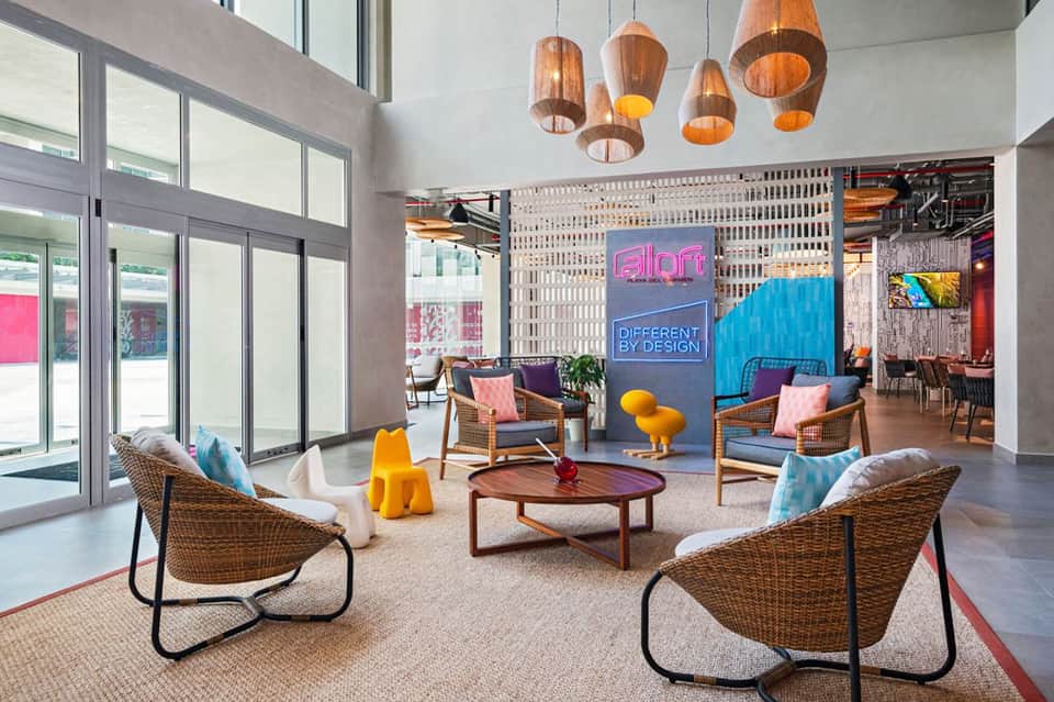 Contemporary hotel lobby with wooden pendant lights, wicker chairs, and colorful modern design