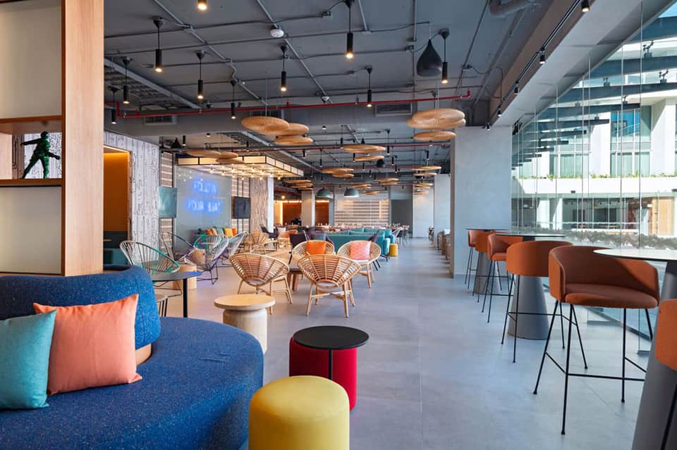 Modern hotel lounge with blue seating, orange accents, hanging pendant lights, and floor-to-ceiling windows