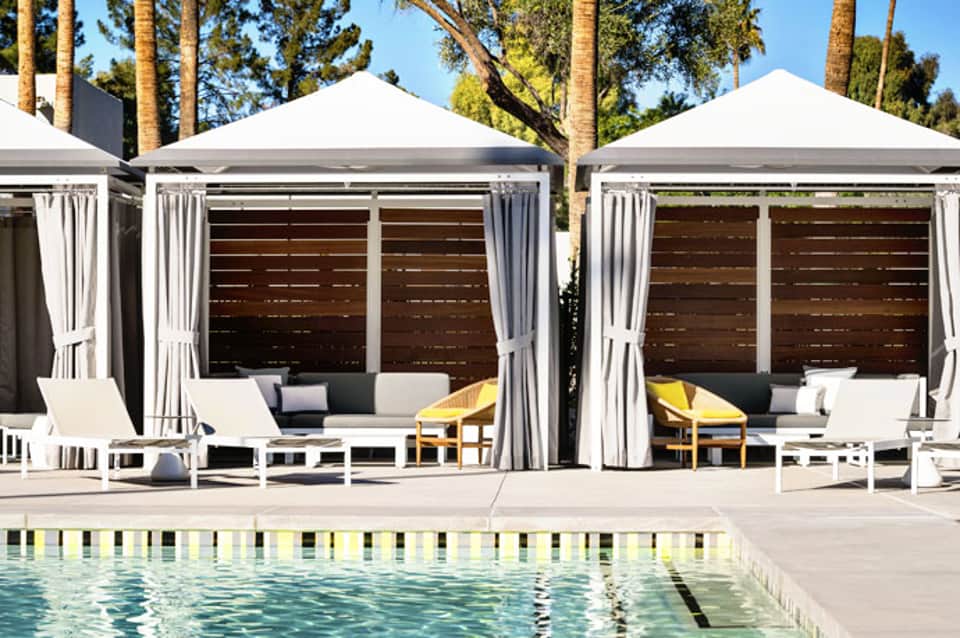 Luxury poolside cabanas with white canopies and lounge seating beside a resort pool and palm trees