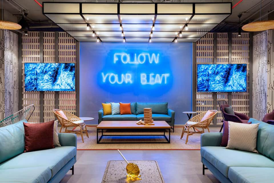 Contemporary hotel lobby with neon blue sign, modern seating, colorful cushions, and accent lighting