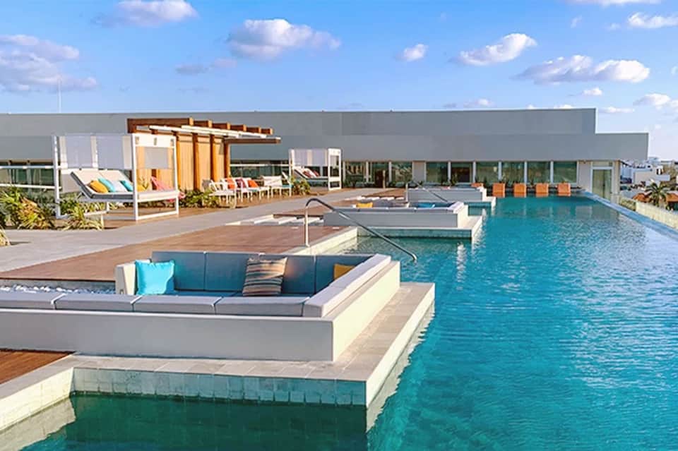 Modern rooftop pool with turquoise water, lounge seating, yellow pergola, and contemporary building