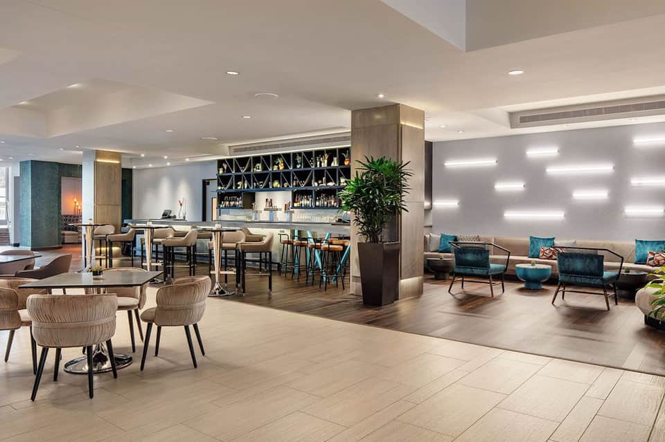 Hotel lobby lounge with bar, modern seating, plants, and contemporary architectural elements
