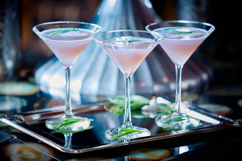 Three pink cocktails with green garnish on black tray at resort bar