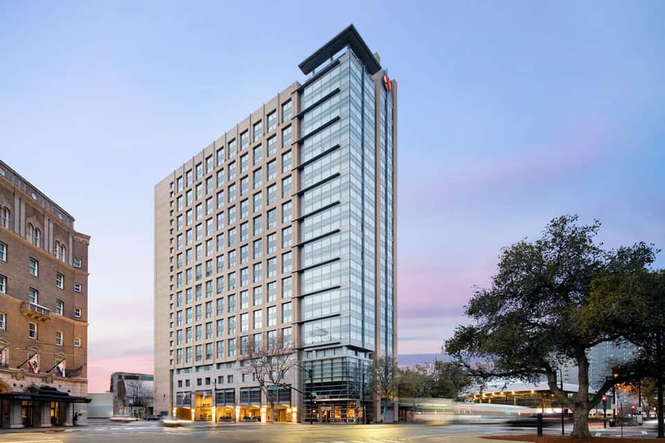 Modern hotel high-rise building with tan and glass facade at dusk with street-level retail