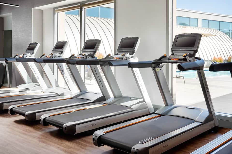 Fitness center with treadmills facing floor-to-ceiling windows overlooking ocean and pool deck
