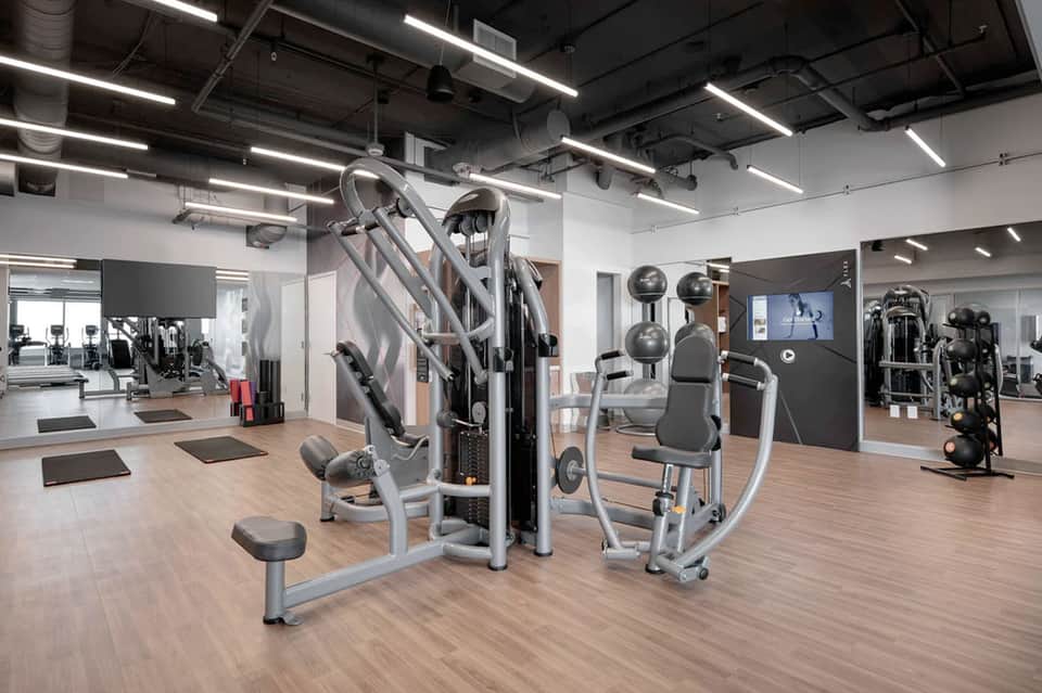 Modern fitness center with exercise equipment, wooden flooring, and bright overhead lighting