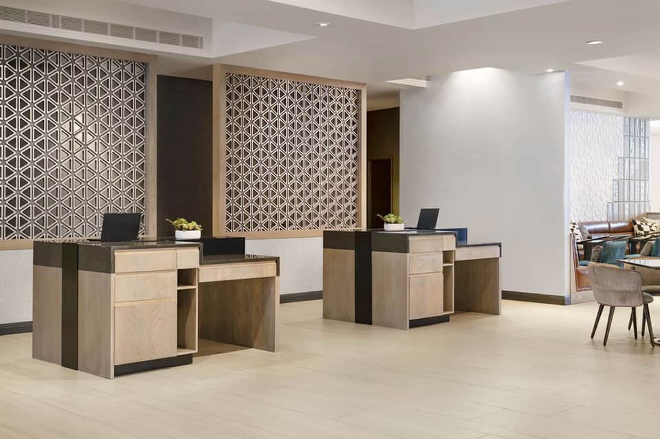 Contemporary hotel check-in desk with geometric wood screen, light oak cabinetry, and modern seating