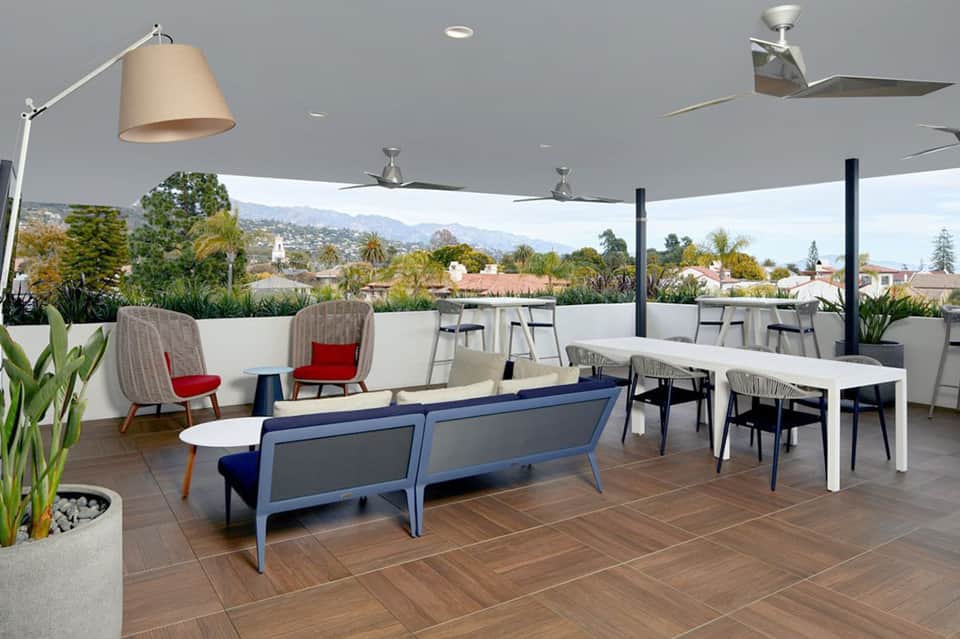 Modern rooftop lounge area with contemporary furniture, shade structures, and scenic mountain views