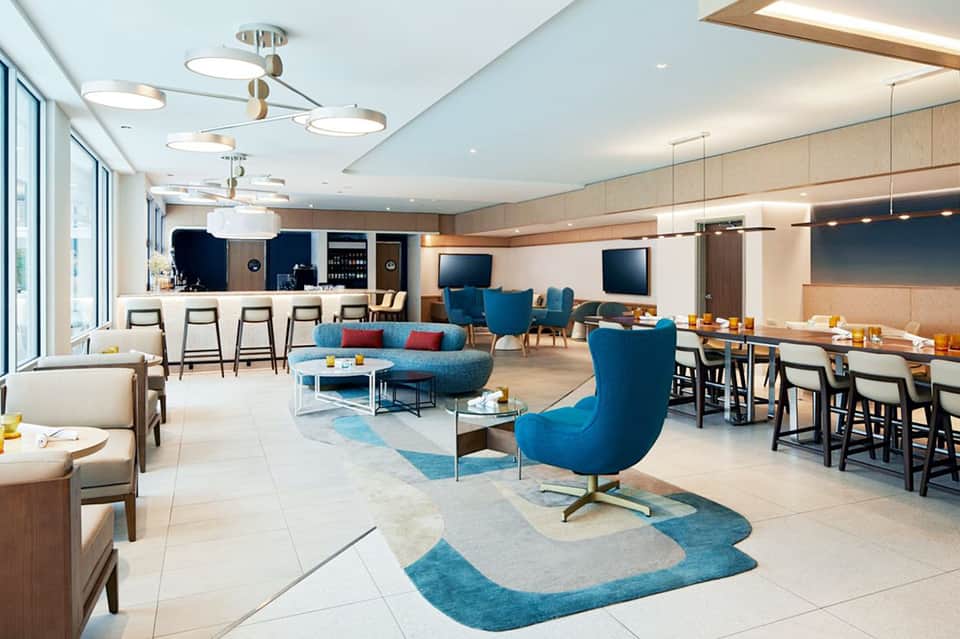 Modern hotel lounge with blue accent furniture, bar, dining area, and contemporary ceiling design