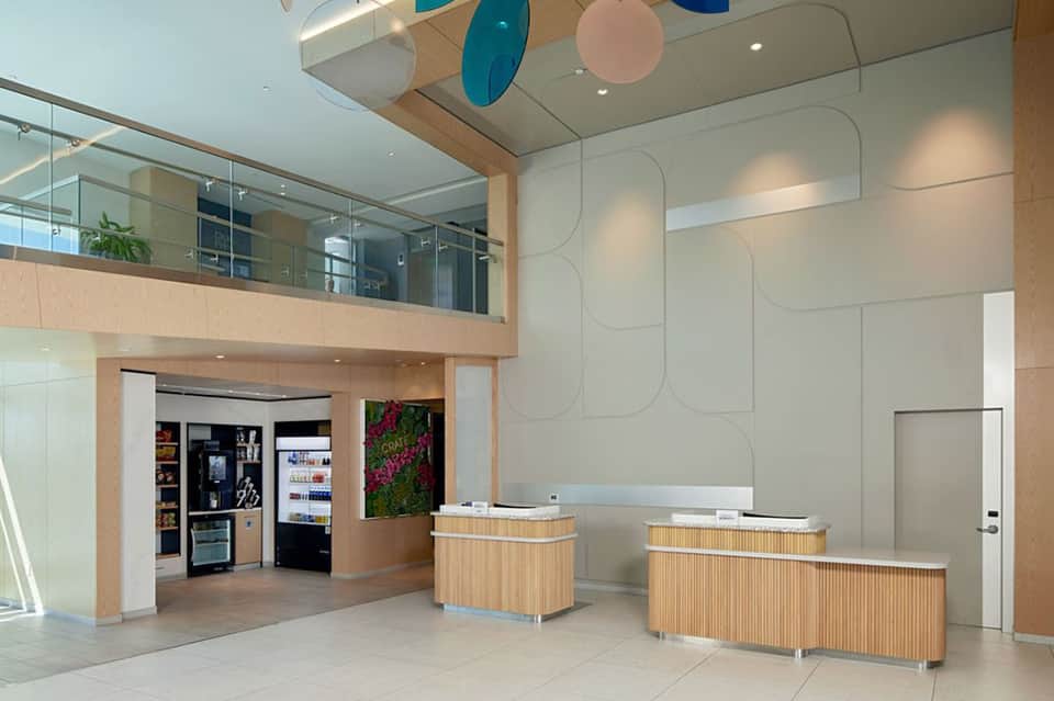 Modern hotel lobby with dual check-in desks, wood accents, and multi-colored ceiling art installation