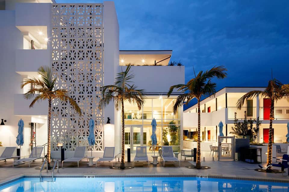 Modern resort pool at night with white lattice architecture, lounge chairs, and palm trees