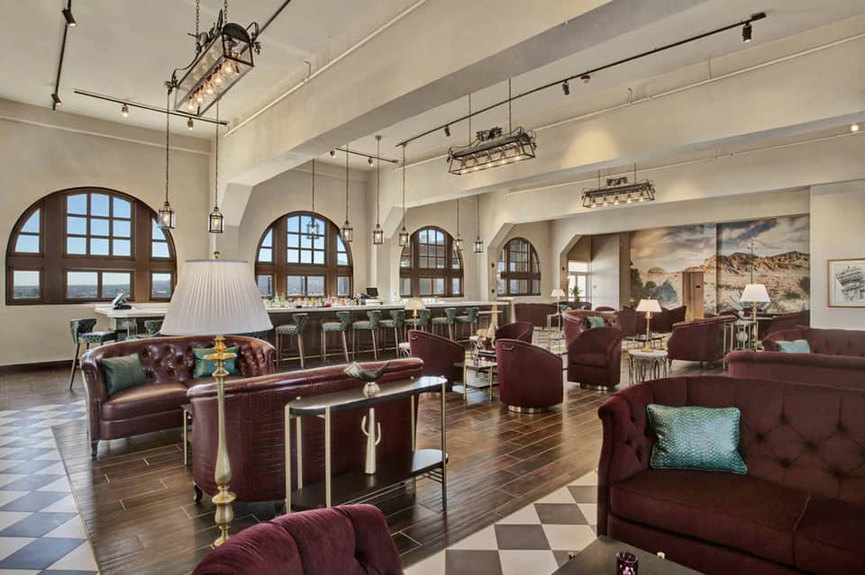 Elegant hotel lounge with burgundy leather seating, arched windows, and classic pendant lighting