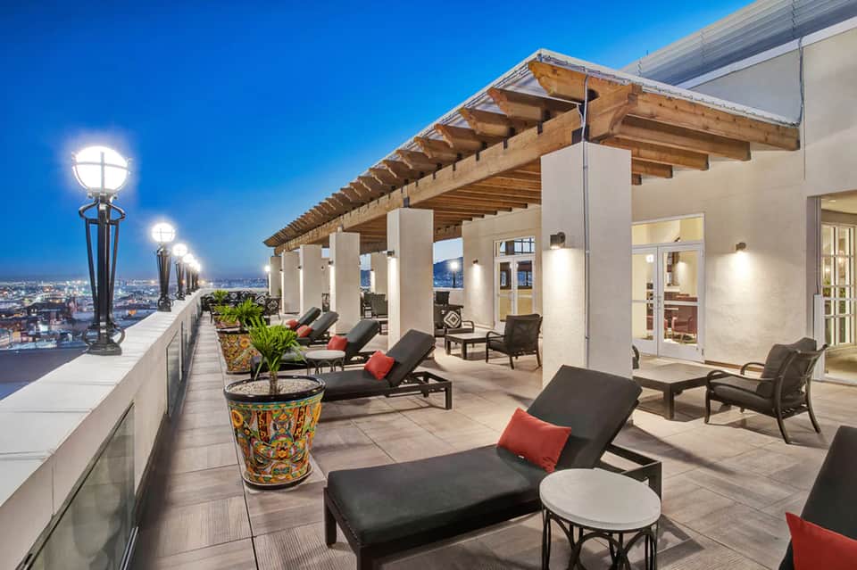 Upscale rooftop terrace with lounge seating, wooden pergola, and downtown city views at dusk