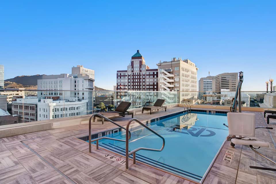 Rooftop pool with city skyline views, lounge chairs, and urban landscape in background during clear day