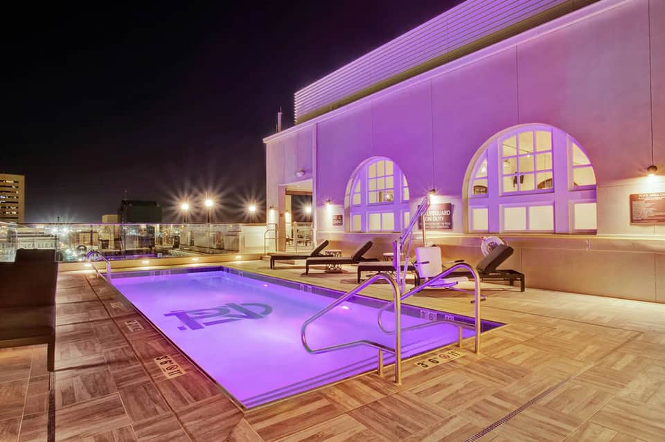 Rooftop pool glowing purple at night with city skyline in background