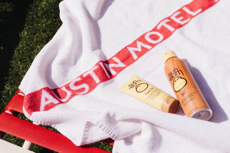 Sunscreen products on white towel with red "Australian Motels" branding on grass background