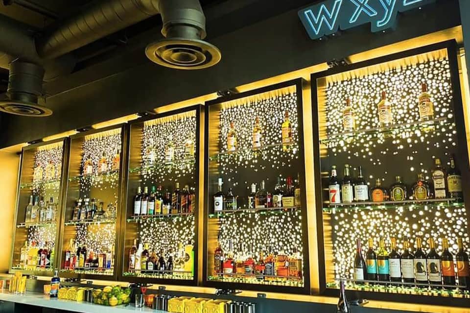 Illuminated bar shelves displaying bottles with decorative pearl-dotted backlit wall panels