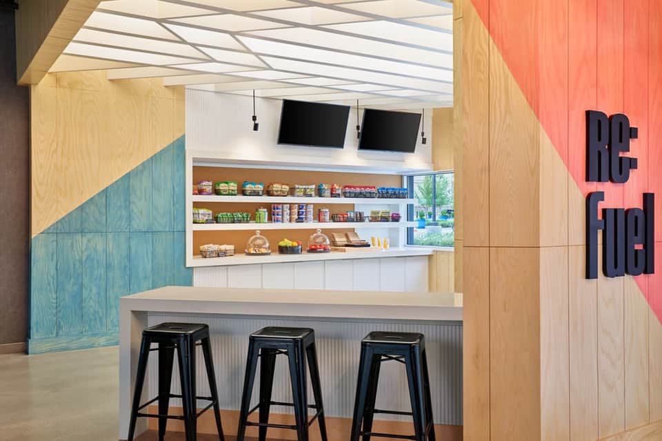 Modern hotel snack bar with colorful geometric walls, shelving, and bar seating