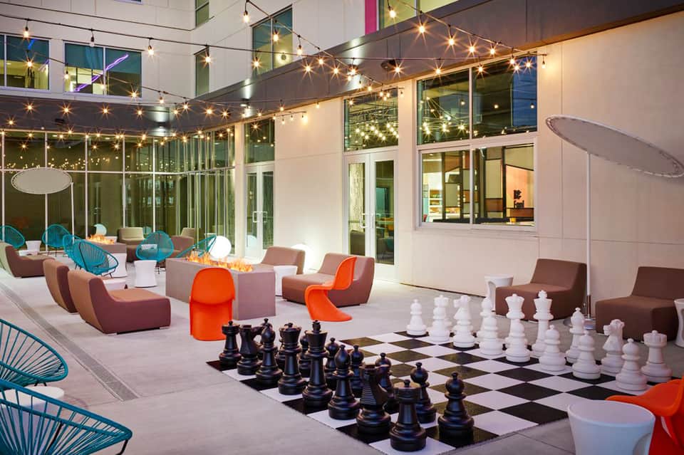 Outdoor courtyard lounge with modern seating, string lights, and giant chess game