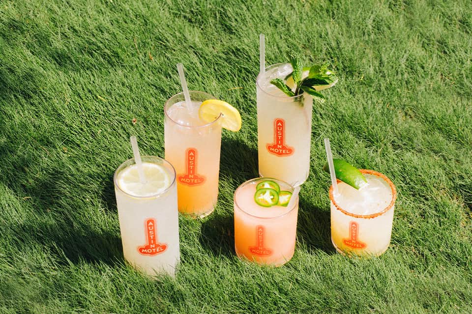 Five colorful cocktails with various garnishes on artificial grass with Motel branding