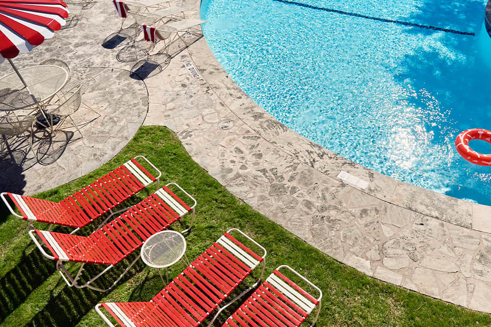 Red and white striped lounge chairs on green grass next to sparkling blue swimming pool