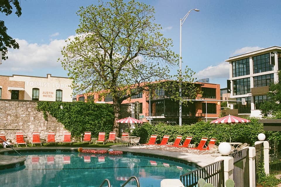 Resort pool with red lounge chairs, hedges, and historic brick buildings