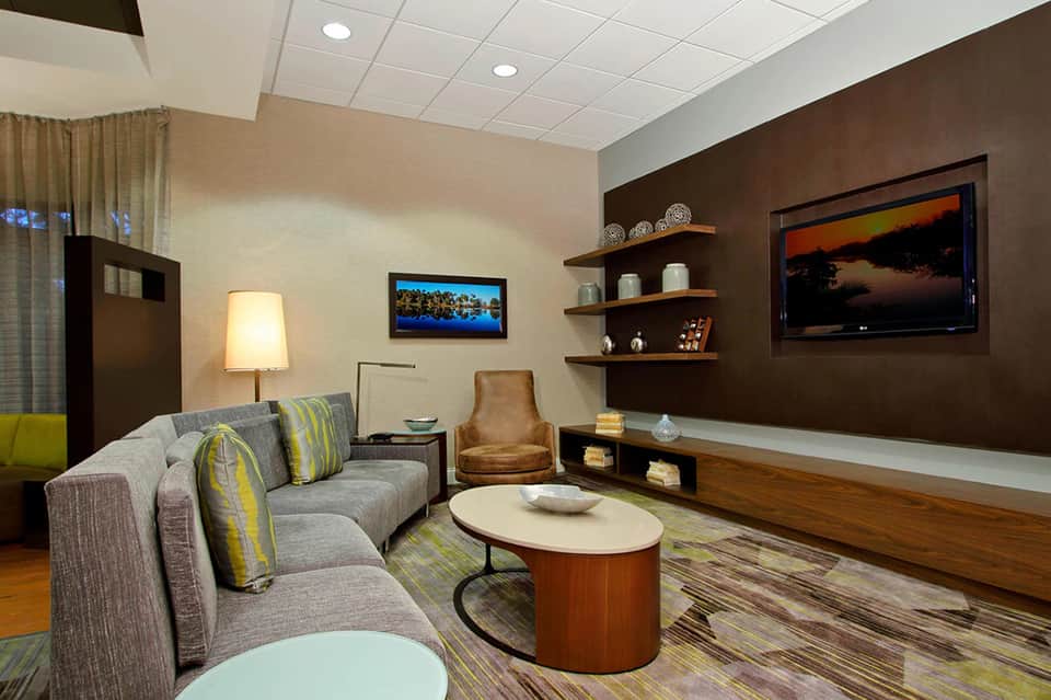 Modern hotel media room with gray sectional sofa, entertainment center, and warm wood accents